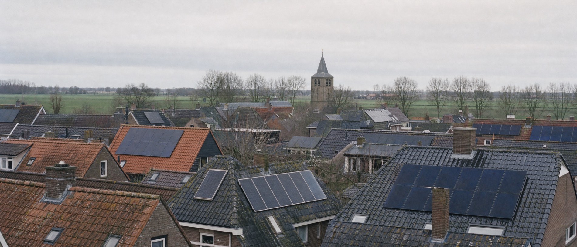 Uitzicht over de daken van een Fries dorp onder een bewolkte hemel. Op ongeveer de helft van de pannendaken liggen zonnepanelen.